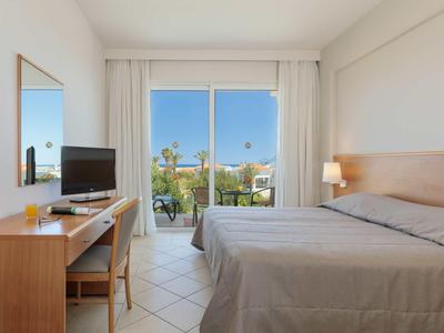 Camera d'hotel luminosa con letto matrimoniale, scrivania, TV e balcone con vista sul verde.