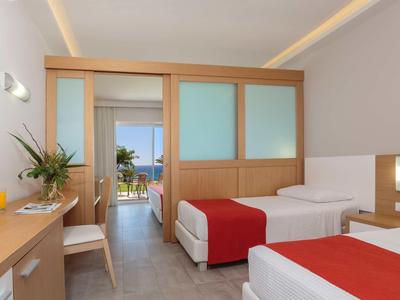 Camera d'hotel moderna con due letti singoli, coperte rosse, mobili in legno e vista sul balcone.