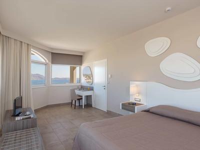 Camera d'hotel luminosa con letto matrimoniale, scrivania e grande finestra con vista sulle montagne.