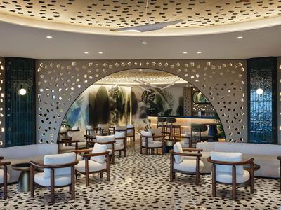 Elegante Hotelbar mit runden Tischen, bequemen Stühlen und dekorativer Wandbeleuchtung.