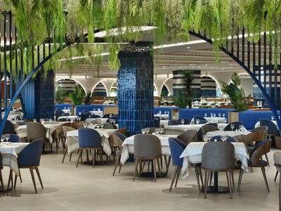 Elegantes Restaurant mit blauen Stühlen und weißen Tischen unter grünem Blätterdak.