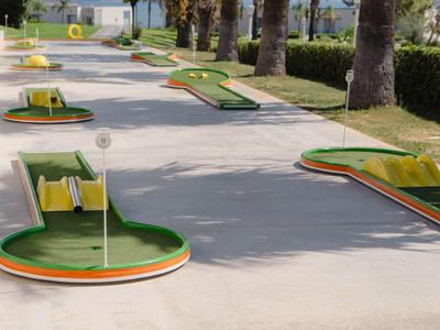 Minigolfanlage mit mehrfarbigen Bahnen auf Beton unter Palmen am Hotel.