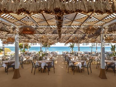 Offenes Restaurant mit gedeckten Tischen und Blick auf das Meer unter einem dekorativen Dach aus Naturmaterialien.