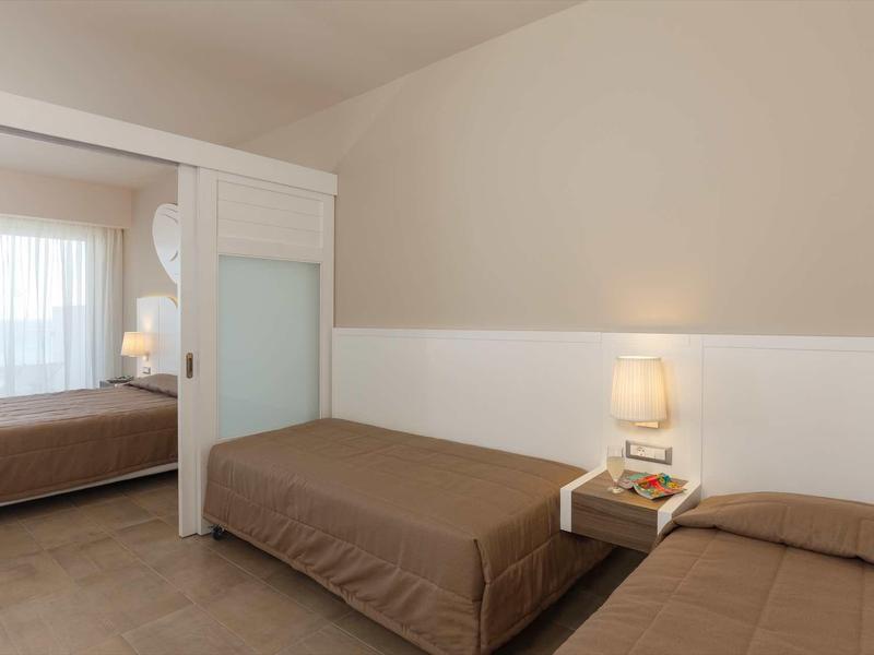 Camera d'hotel moderna con due letti singoli, biancheria marrone e comodino con lampada.