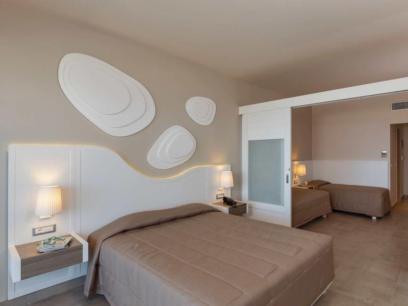 Camera d'hotel moderna con due letti, comodini, lampade e decorazione murale morbida.