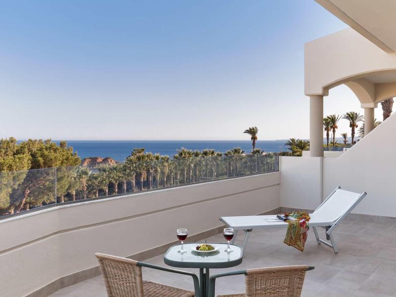 Balcone con tavolo, sedie e sedia a sdraio con vista su palme e oceano.