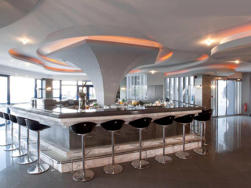 Bar moderno in hotel con sgabelli alti e grandi finestre che offrono luce naturale.