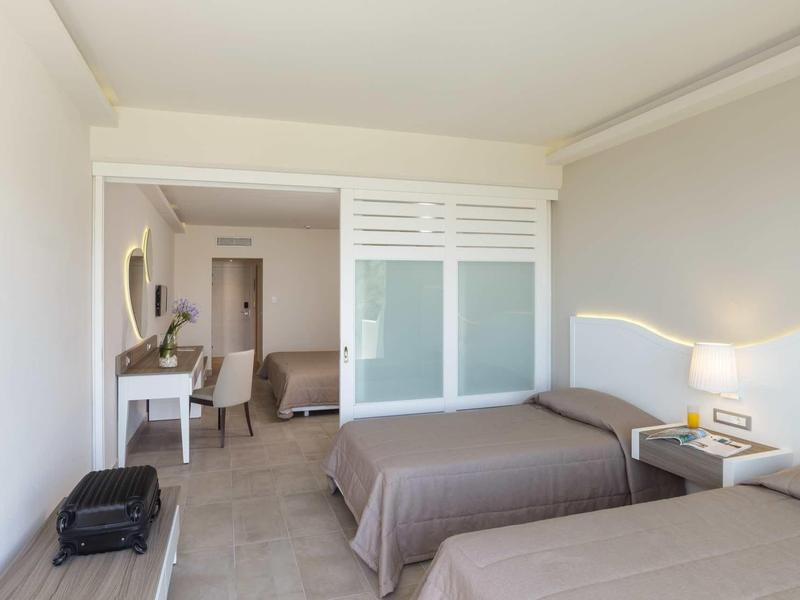 Camera d'albergo con due letti, lampada da comodino, scrivania, sedia e porte scorrevoli in vetro smerigliato.