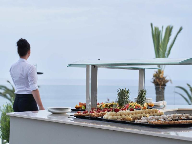 Tavolo buffet con vari cibi con vista sull'oceano e palme.