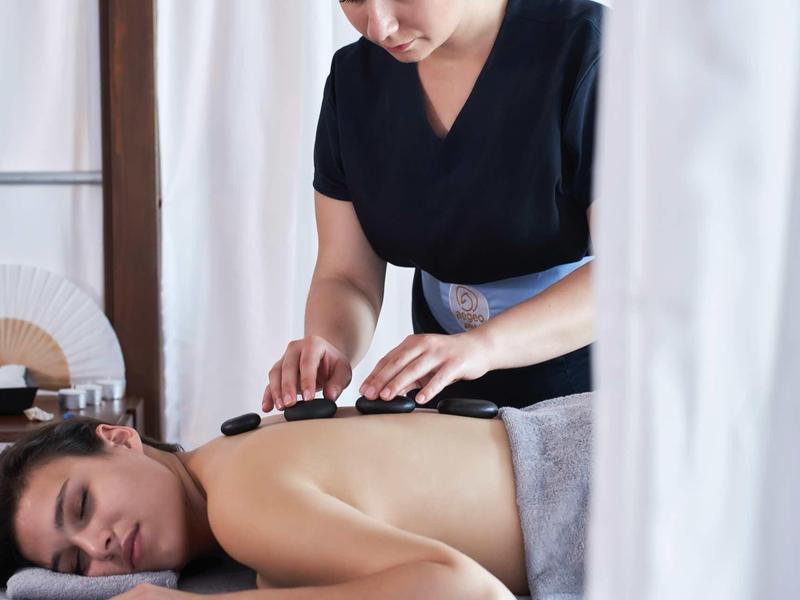 Persona che riceve un massaggio con pietre calde in una tranquilla stanza spa con luce naturale.