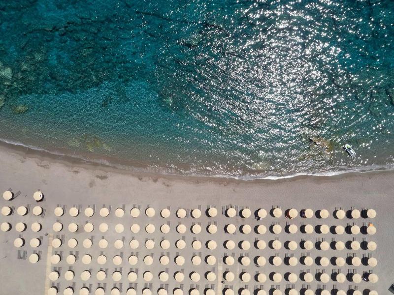 Vista aerea di una spiaggia con file di ombrelloni bianchi vicino ad acqua turchese limpida.