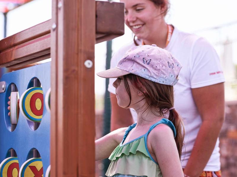 Bambina gioca a un gioco interattivo da parete sotto sorveglianza adulta all'aperto.