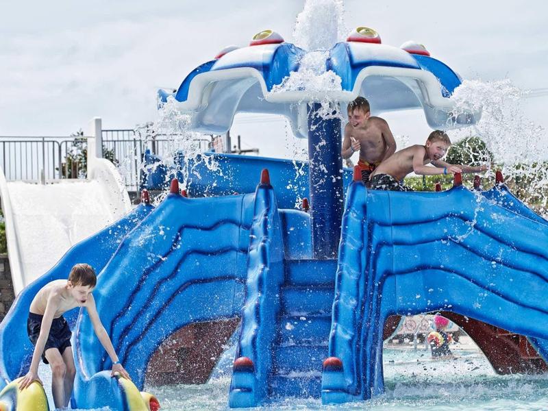 Bambini che giocano su uno scivolo d'acqua blu con ombrello spruzzante e fontana in piscina.