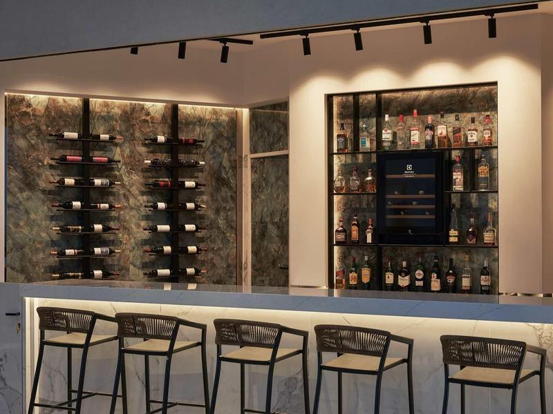 Bar moderno dell'hotel con bancone in marmo, sgabelli alti e scaffali illuminati di vini e liquori.