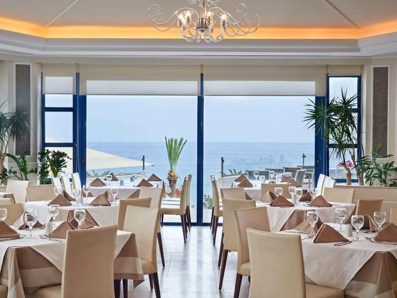 Ristorante luminoso ed elegante con vista sull'oceano e tavoli ordinati con tovaglie bianche.