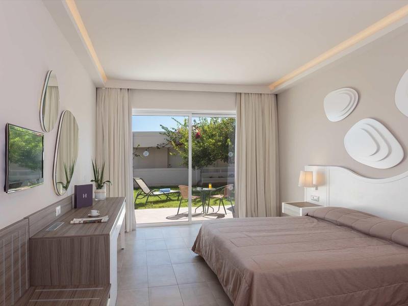 Camera d'albergo moderna con letto matrimoniale, specchi a muro, TV e porta scorrevole sul giardino.