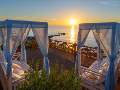 Two cozy beds with white mosquito nets at sunset by the sea.