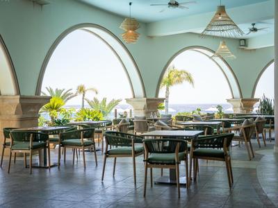 Offener Gastronomiebereich mit Stühlen, Tischen und Blick auf Palmen und Meer.