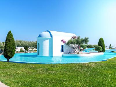 White building with blue roof in center of pool, surrounded by grass and trees.