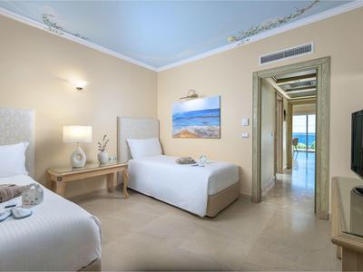 Lichte hotelkamer met twee eenpersoonsbedden, elegante inrichting en uitzicht door de deur op terras en zee.