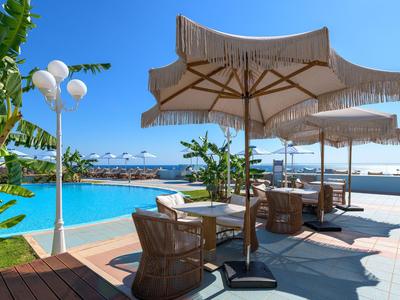 Pool area with sun umbrellas, chairs, and view of the sea under clear sky.