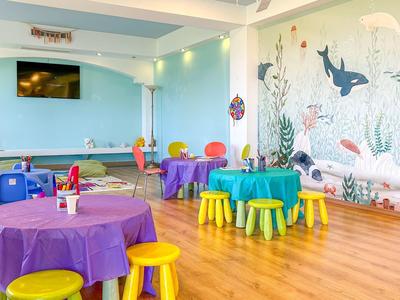 Kleurrijke kinder speelruimte met kleine tafels en krukken, muur versierd met maritieme motieven.