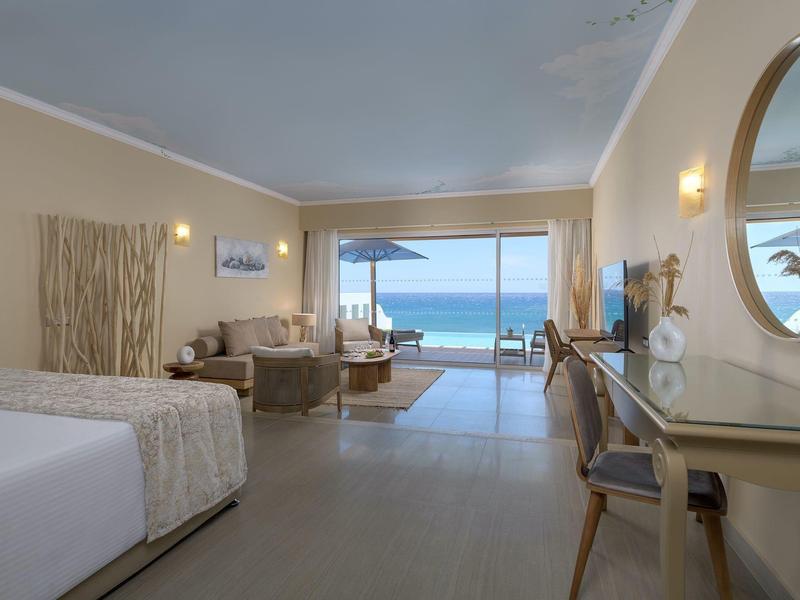 Ruime hotelkamer met zithoek en uitzicht op de oceaan door grote schuifdeuren.