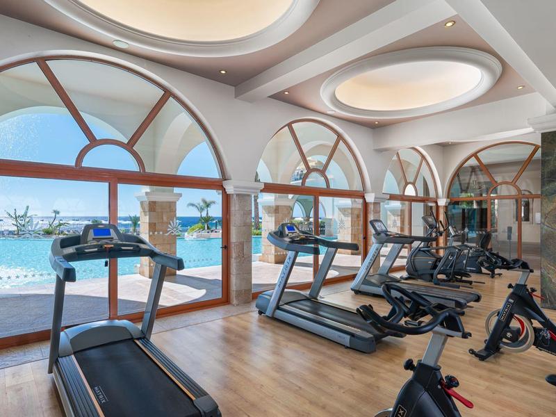 Lichte sportschool met grote ronde ramen met uitzicht op de jachthaven, uitgerust met loopbanden en hometrainers.