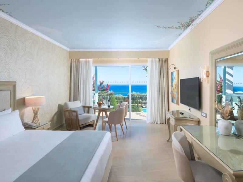 Lichte hotelkamer met tweepersoonsbed, balkon en zeezicht.