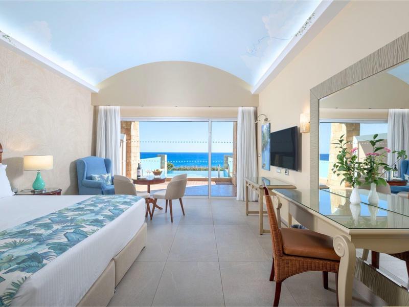 Lichte hotelkamer met zeezicht, tweepersoonsbed, zitgedeelte en elegante bureau.