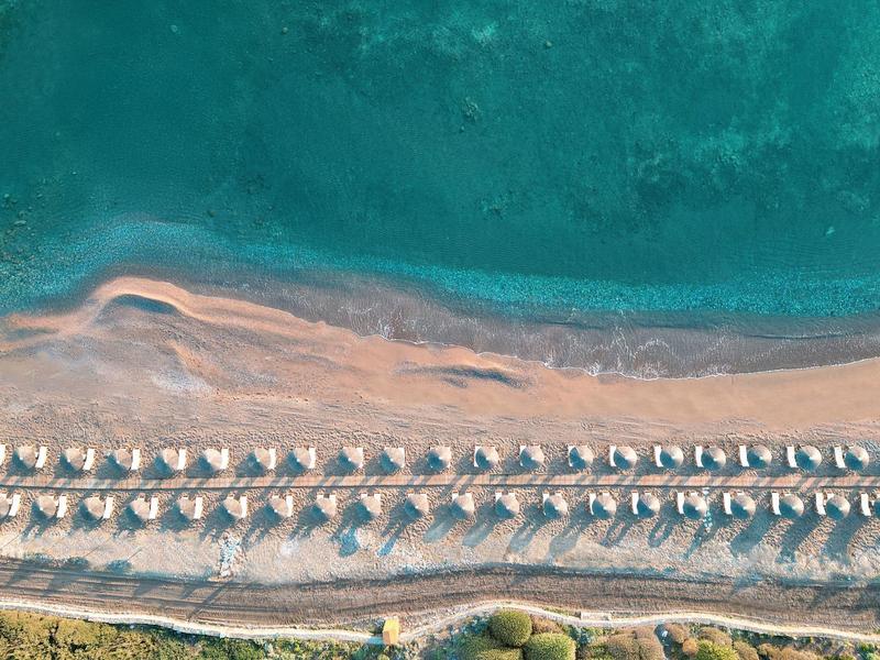 Luchtfoto van een strand met twee rijen parasols en ligbedden langs het water.
