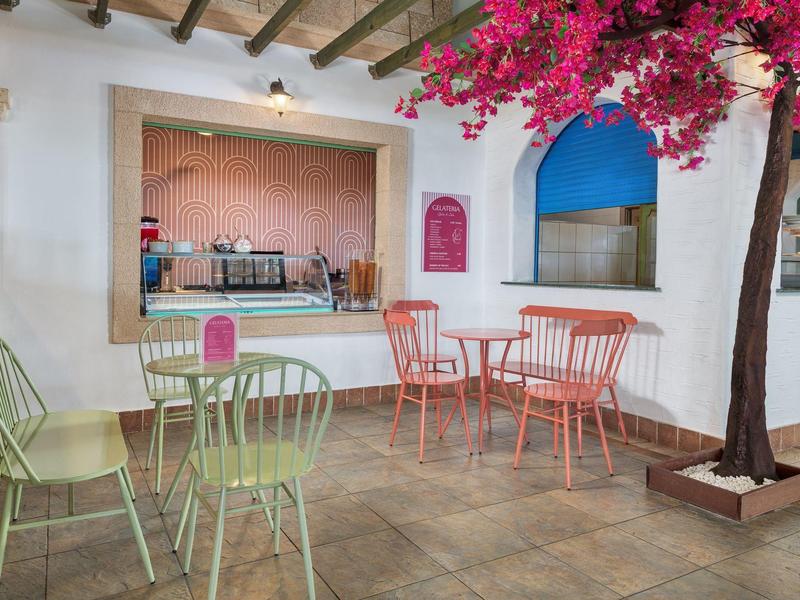 Knusse caféhoek met kleurrijke stoelen en een kunstboom binnen.