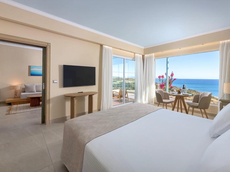 Lichte hotelkamer met tweepersoonsbed, balkon en zeezicht bij daglicht.