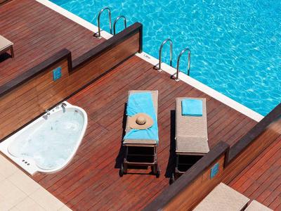 Holzdeck mit Liegestühlen und Jacuzzi neben einem blauen Pool im Freien.