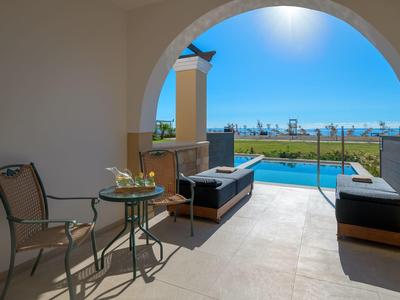 Terrasse mit Sitzgelegenheit, Blick auf Pool und Meer unter blauem Himmel.