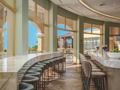 Interno di un bar luminoso ed elegante con bancone in marmo e sgabelli accoglienti vicino a grandi finestre.