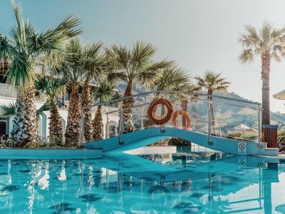 Piscina con fontane, ponti blu e palme in una struttura alberghiera con sole