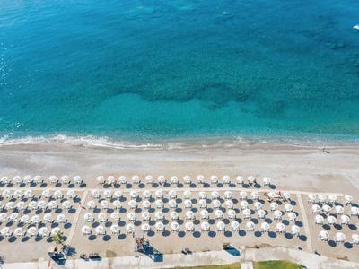 Vista aerea di una spiaggia con file di ombrelloni e acqua azzurra e limpida.