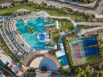 Luftaufnahme eines Hotelpools mit Wasserrutschen und Tennisplätzen nebenan.