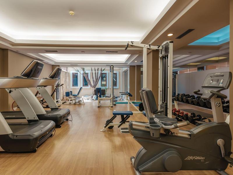 Moderne Fitnessraum mit Laufbändern, Hanteln, Kraftmaschinen und Holzboden in warmem Licht.