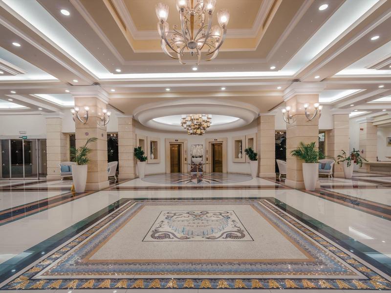 Großer heller Hotellobby mit Marmorfußboden, Säulen, Kronleuchtern und dekorativen Wandspiegeln.