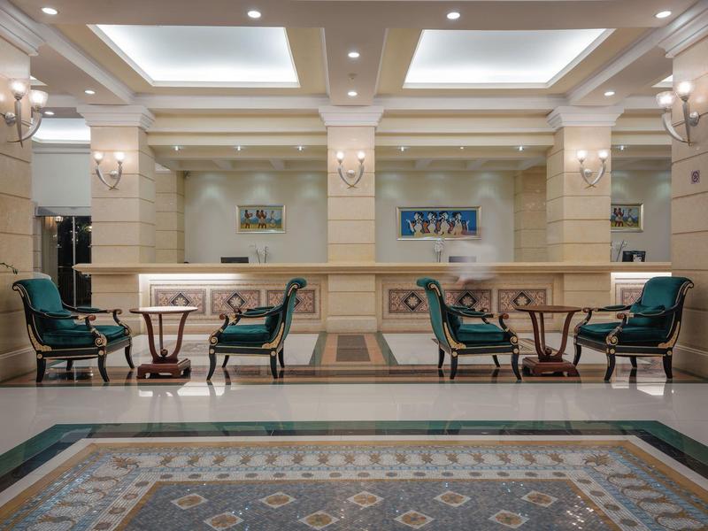 Eleganter Raum mit vier grünen Sesseln, zwei Tischen, marmorne Wände und Decke mit Lichtkästen.