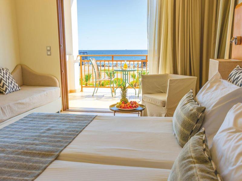 Helles Hotelzimmer mit zwei Betten, Sitzbereich, Balkon und Meerblick bei Tageslicht.