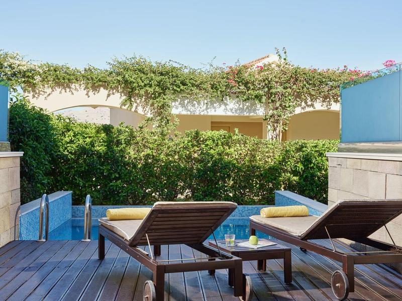 Zwei Liegestühle auf einer Holzterrasse mit Blick auf eine grüne Hecke und Pergola.