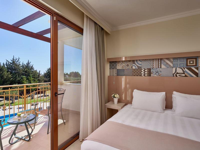 Helles Schlafzimmer mit Doppelbett, Holzmöbeln und Balkon mit Tisch, Stühlen und Blick auf Bäume.