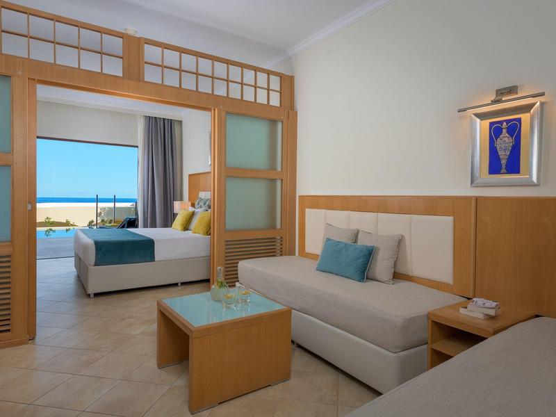 Modernes Hotelzimmer mit Sitzbereich, Bett und Meerblick durch große Fenster.