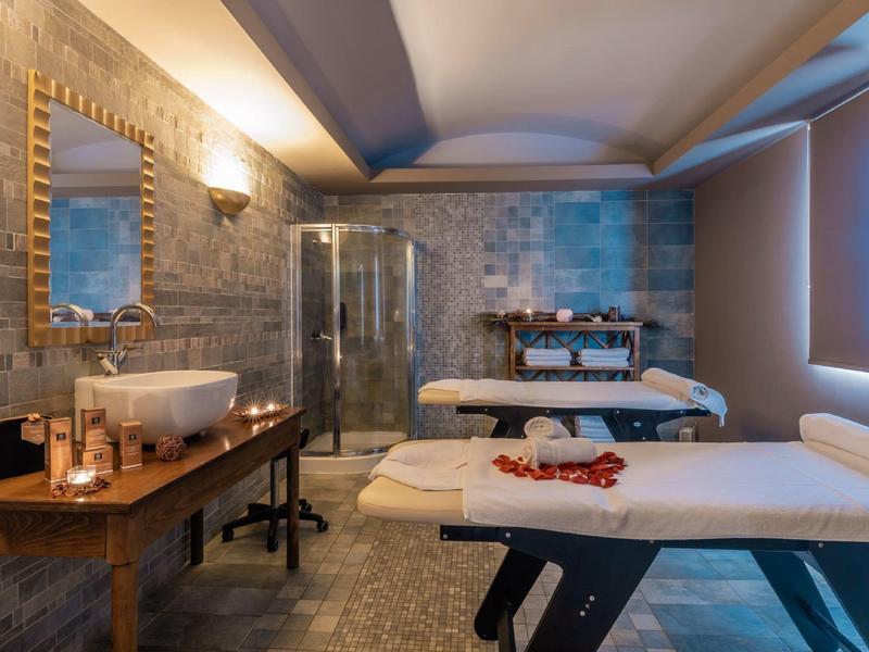 Ein gemütlicher Wellnessraum mit Massageliegen, Spiegel, Dusche und warmem Licht.