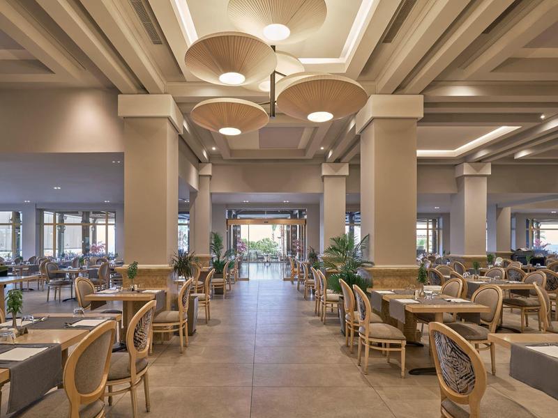 Großer, eleganter Hotelrestaurantbereich mit vielen Tischen und Stühlen unter einer hellen Decke.