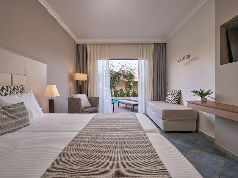 Modern eingerichtetes Hotelzimmer mit Doppelbett, Sofa, TV und Balkontür mit Blick auf Garten.