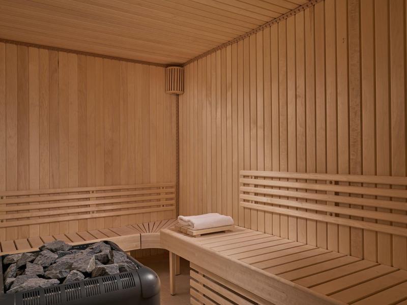 Holzsauna mit Hockbank, Liegebänken und Saunaofen voller schwarzer Steine.